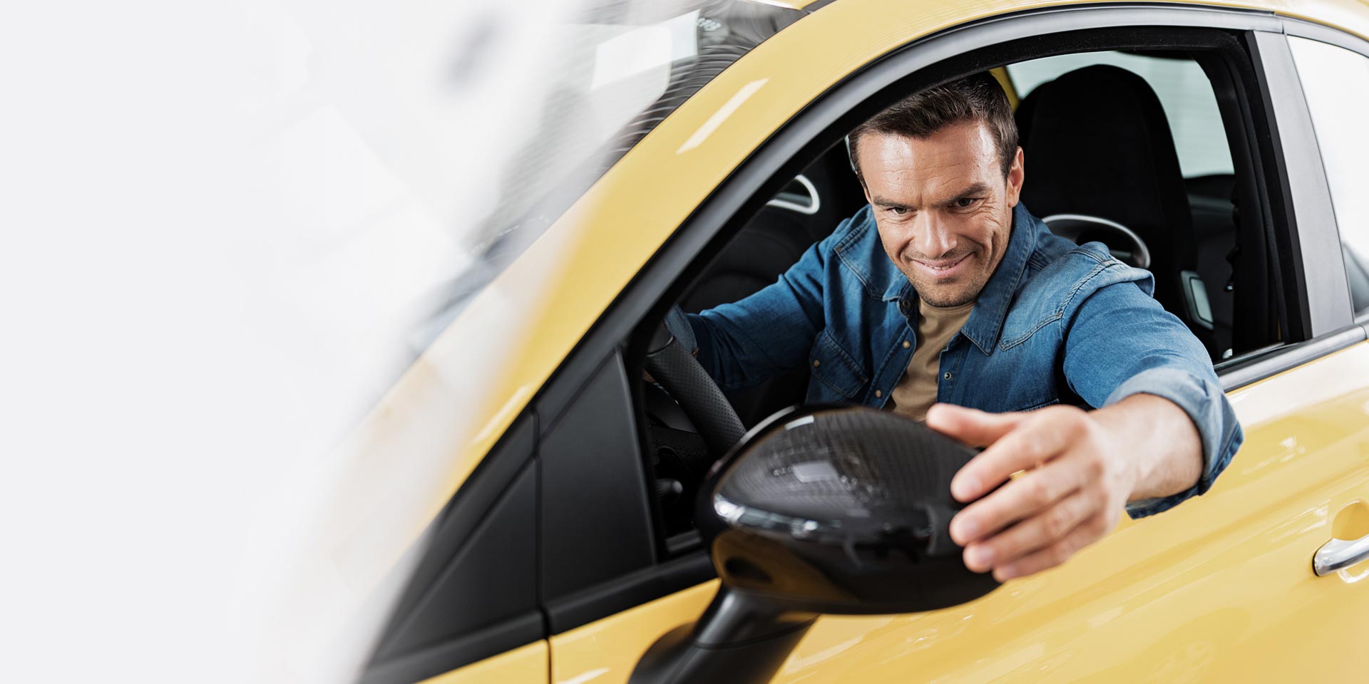 A man looking and smiling in the rear view mirror of his new car that was purchased with an Auto Loan