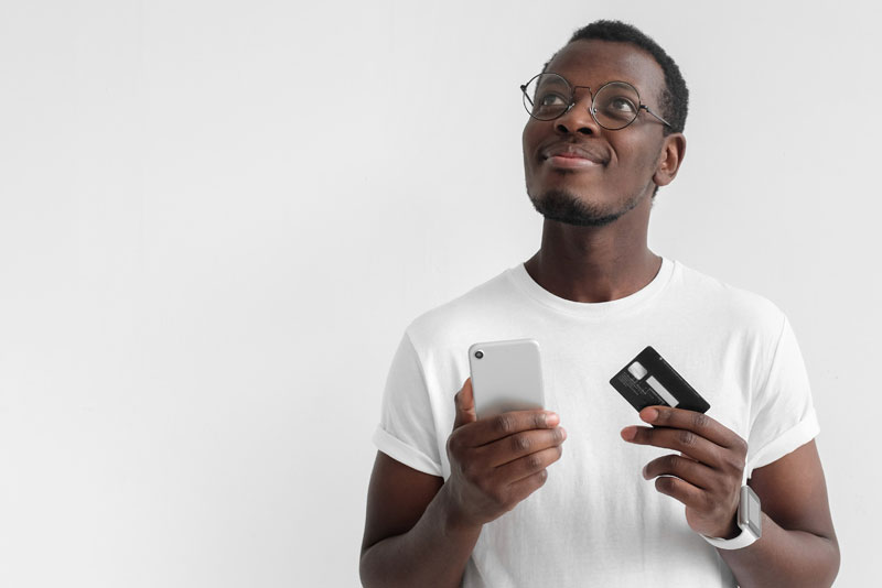 A young man holding a mobile device and a credit card has signed up for eStatements and has gone paperless