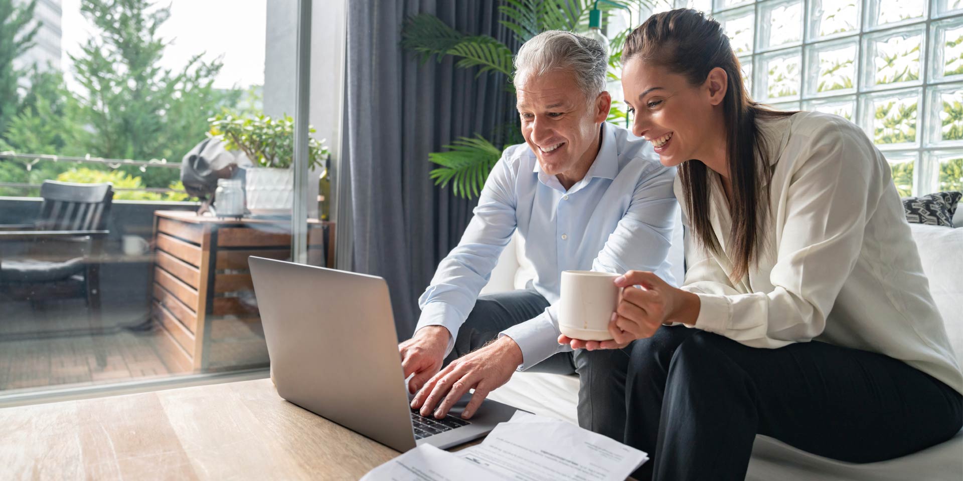 A middle aged couple looking at a laptop are smiling and sitting together while discussing their IRA accounts