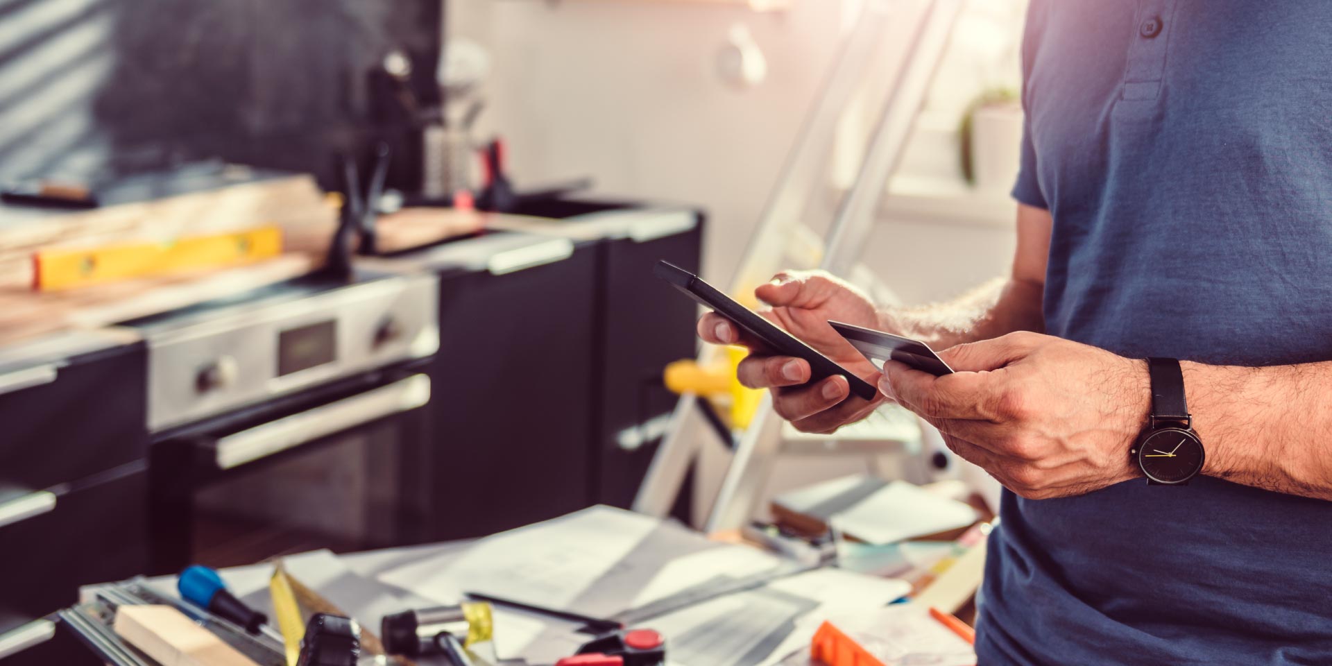 A business owner in his workshop is making a debit card purchase online with his phone