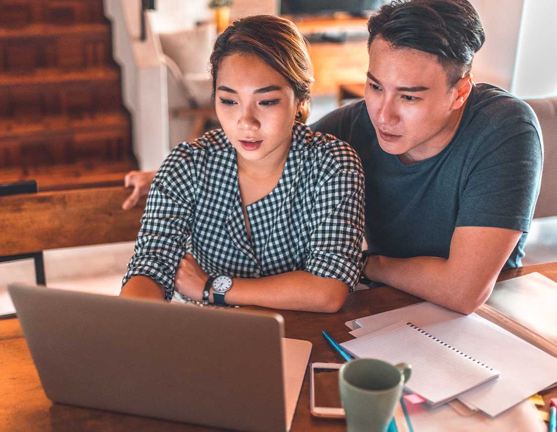 A young couple are developing an investment plan while looking over a laptop and financial documents