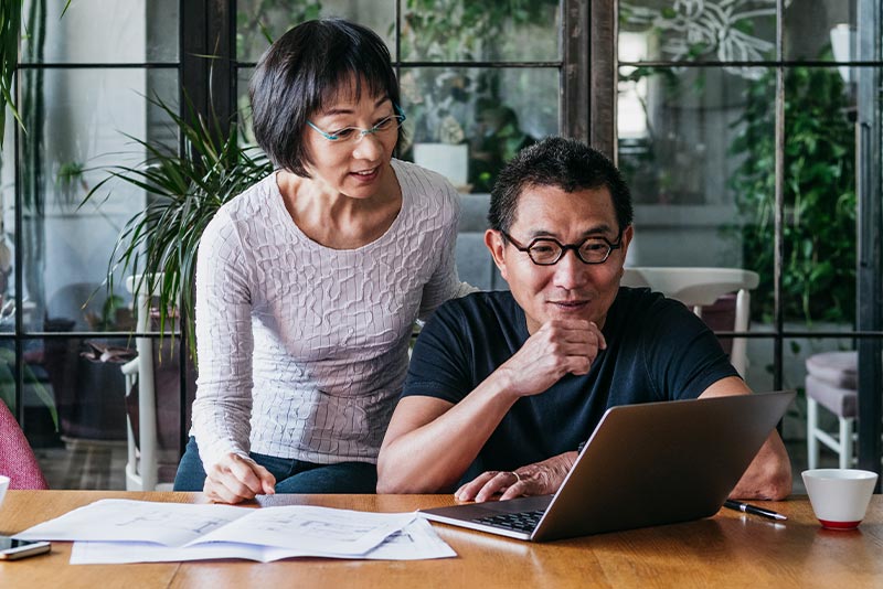 A married couple look over a laptop and financial documents while reviewing their investment plans